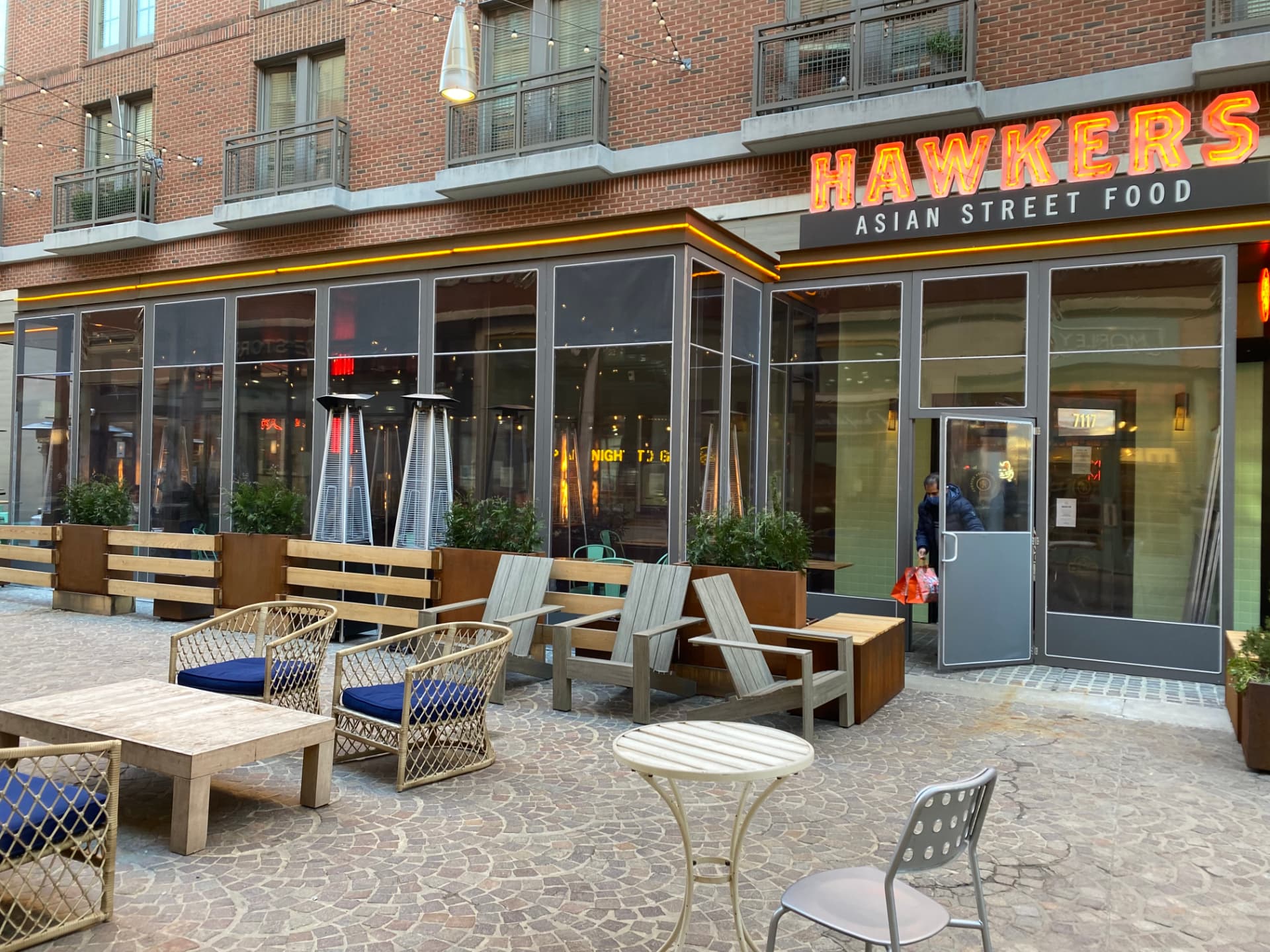Sidewalk dining area with patio seating and heaters outside a restaurant
